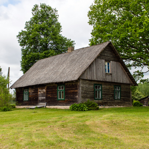 Veca koka viensētas ēka ar zaļiem logiem pie lieliem kokiem